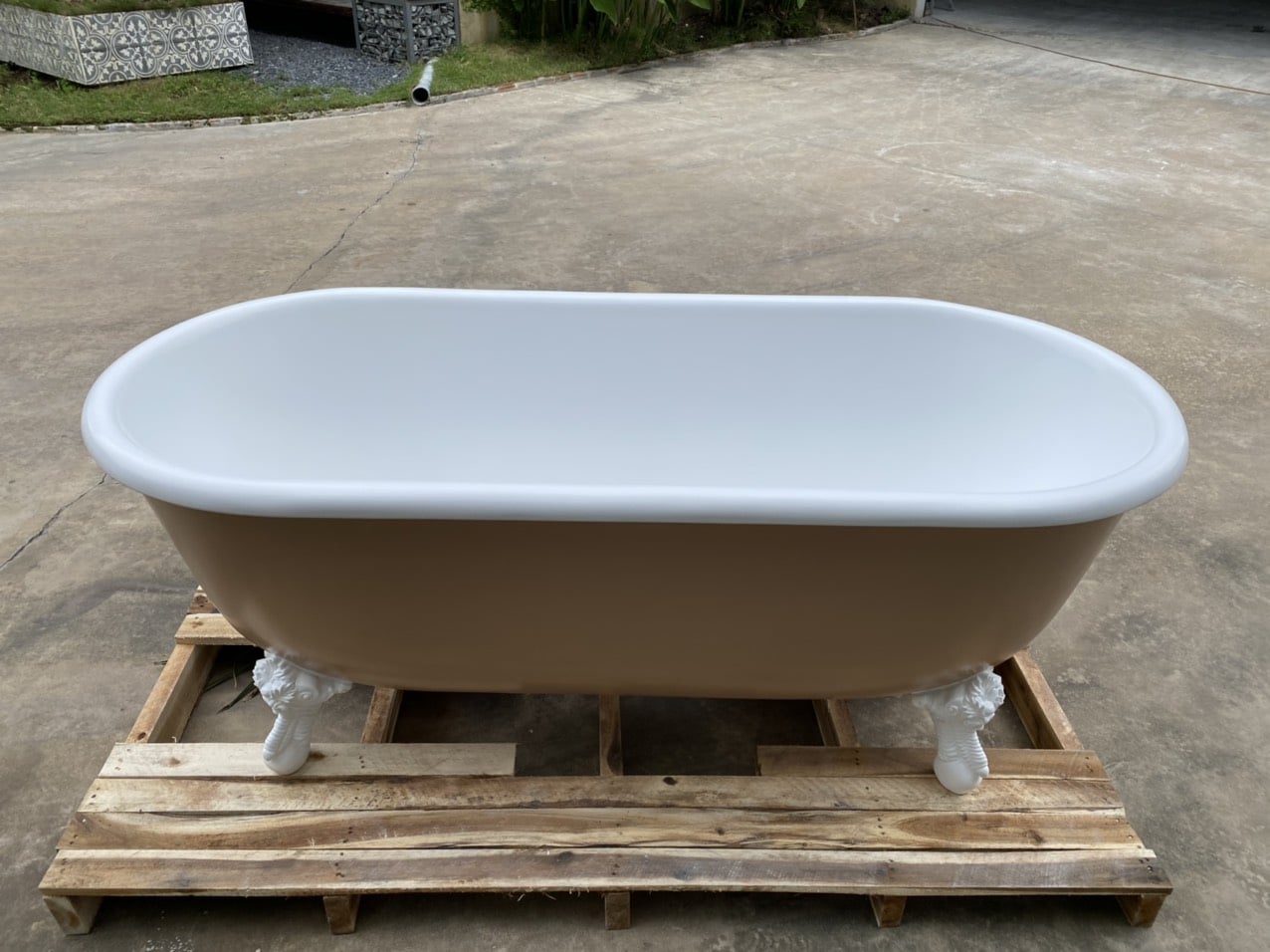 Beige solid surface freestanding bathtub placed on wooden pallet, industrial chic.